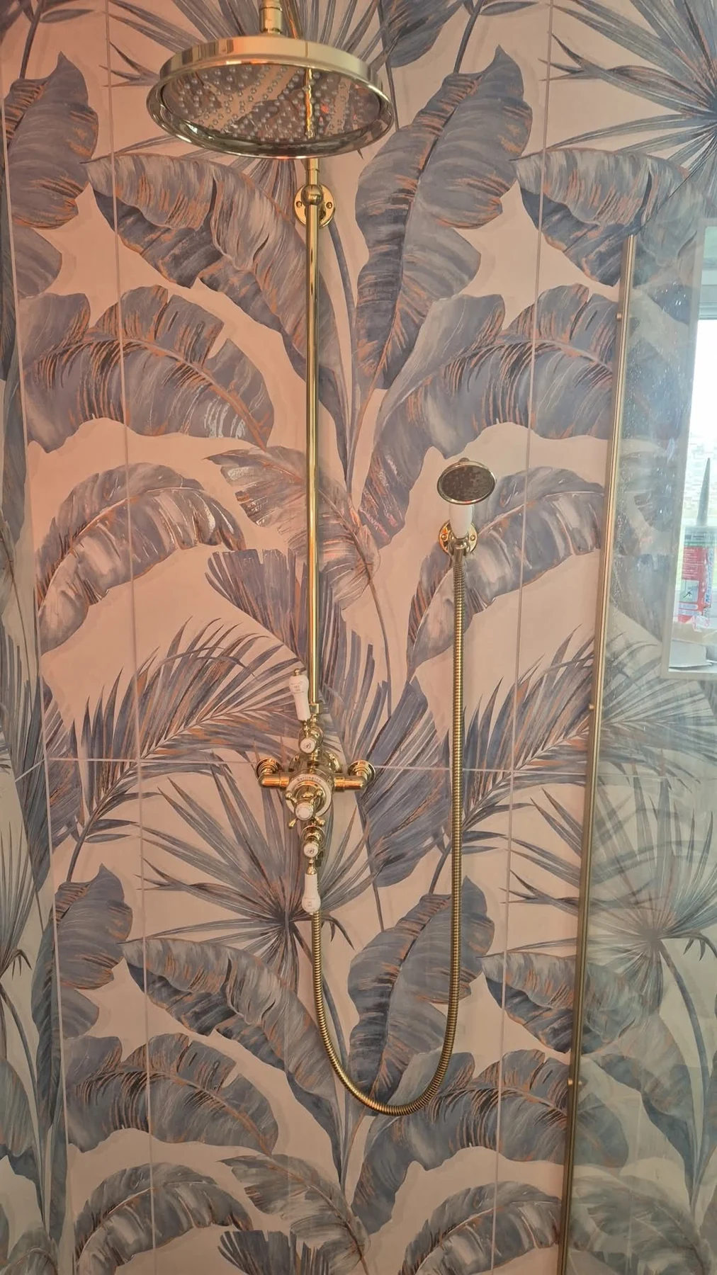 Gold rainfall shower against blue-grey tropical leaf patterned tiles